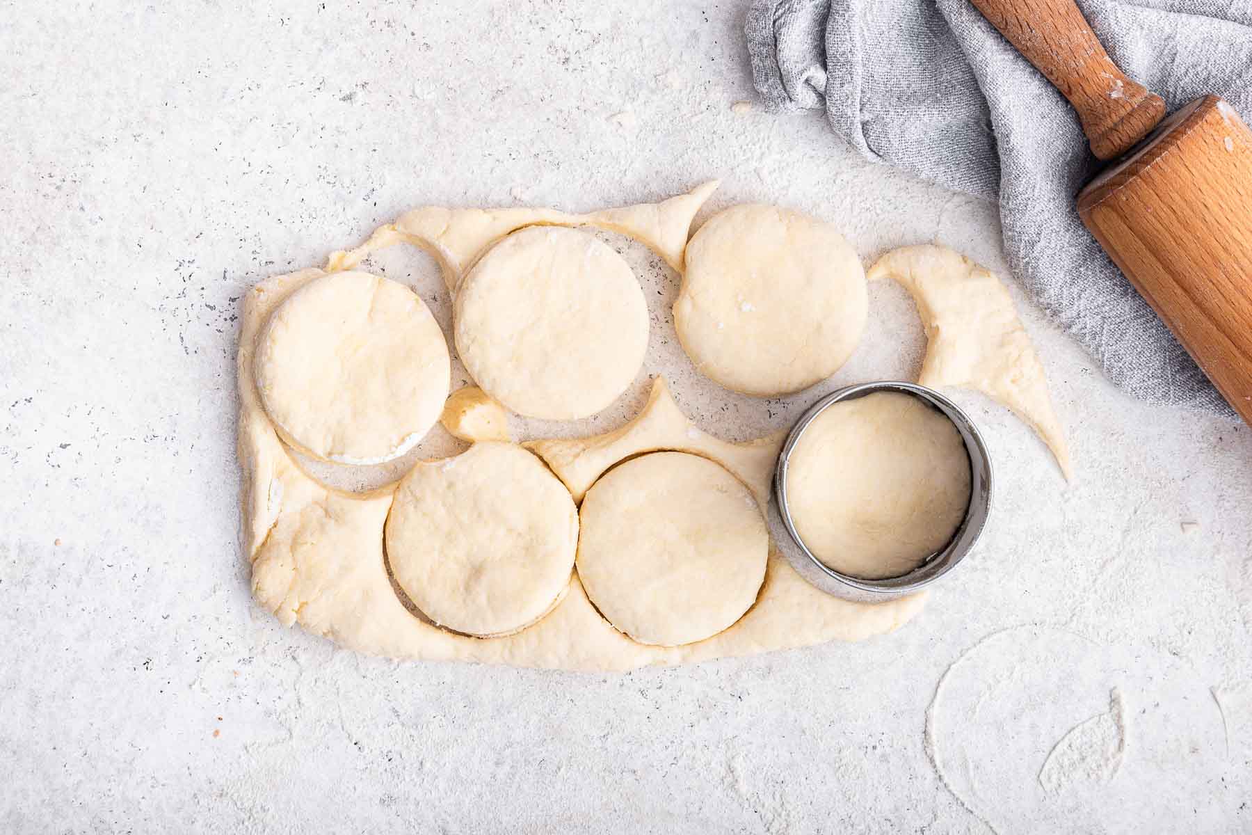 Round cutter making circles in dough on marble block.