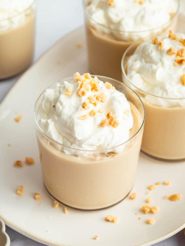 Four glasses full of butterscotch pudding garnished with whipped cream.