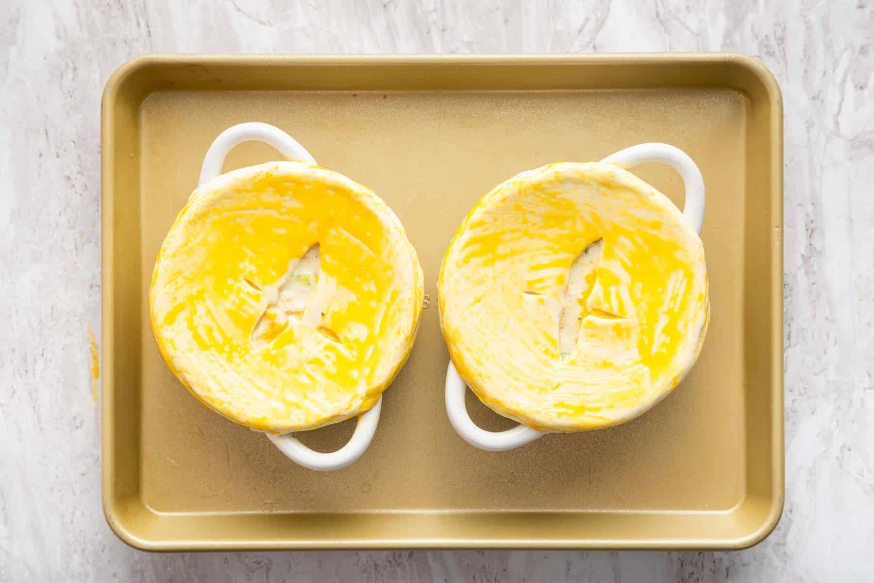 Two bowls with pastry on top brushed with egg yolk.