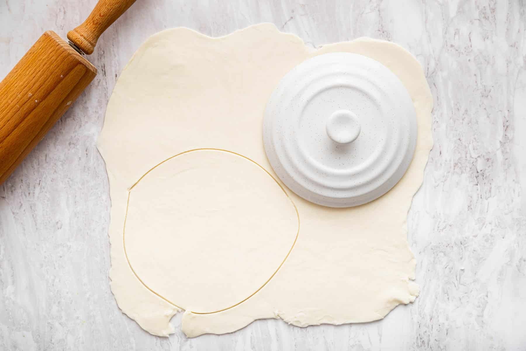 Pastry rolled out with small white lid on top for measuring.