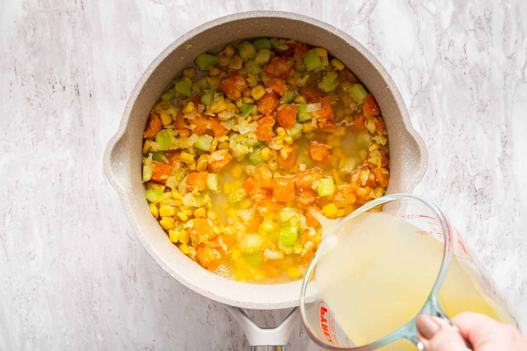 Hand pouring yellow broth into vegetable saute pan.