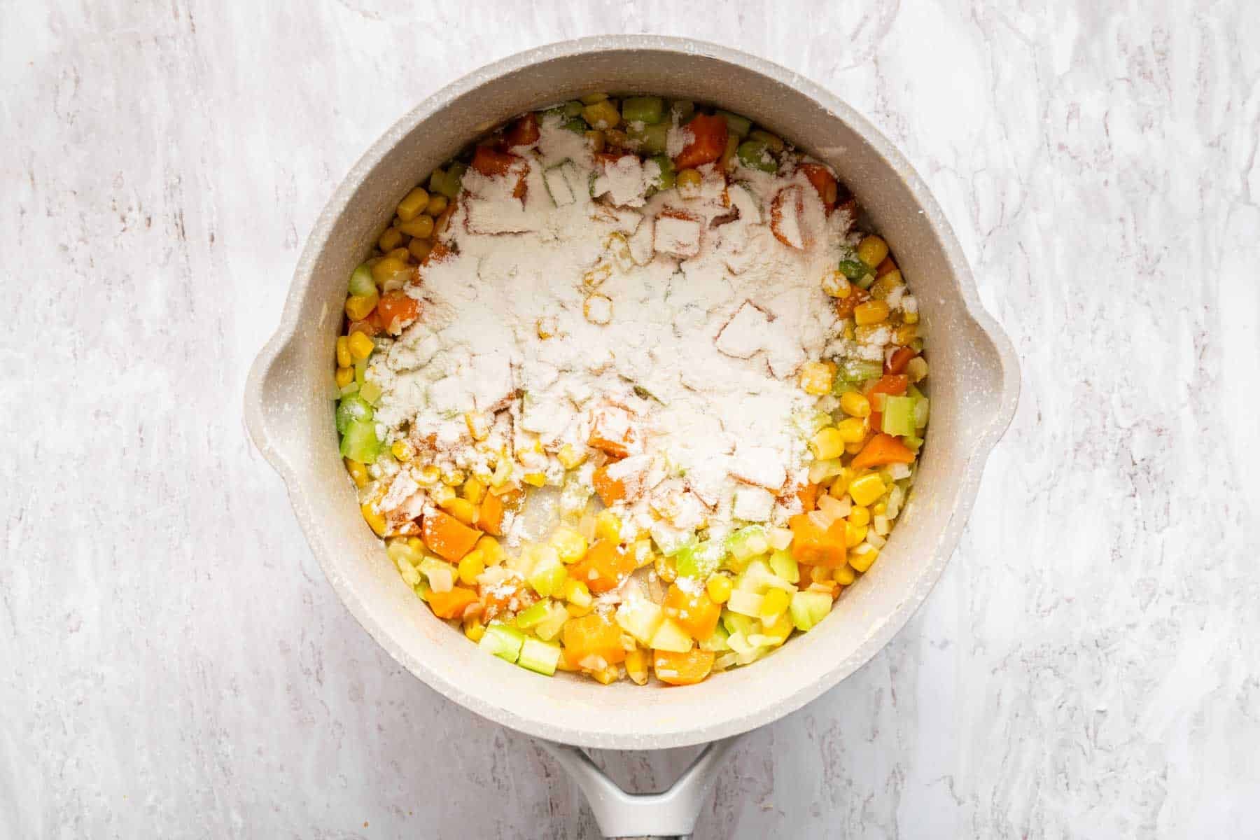 Flour sprinkled over cooked vegetables in a white pan.