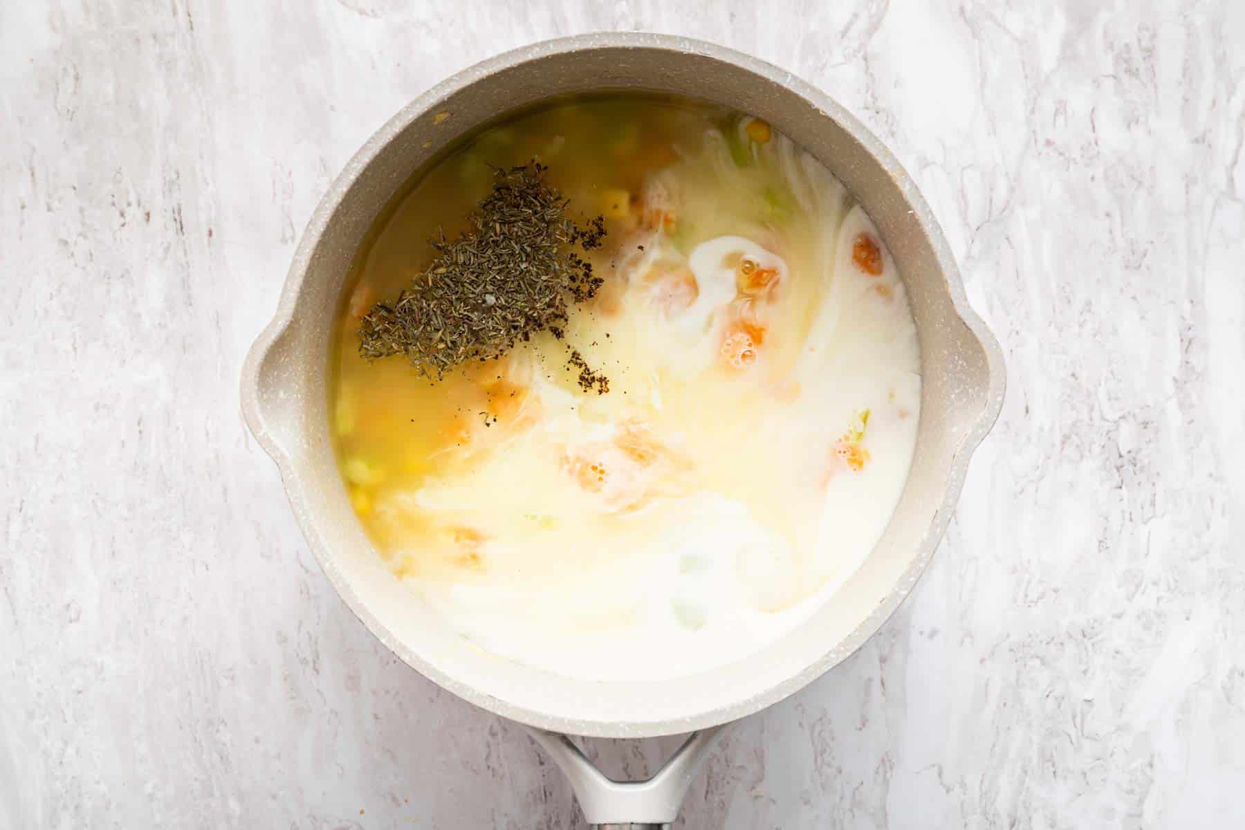 Milky sauce with dried thyme on top in saucepan.