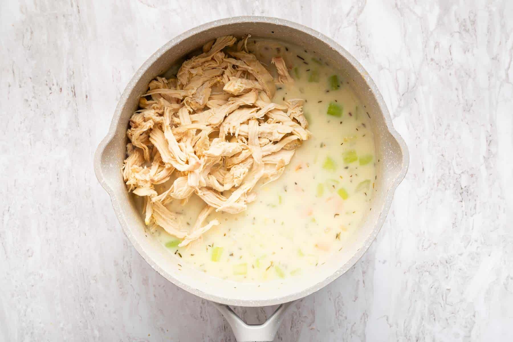 Shredded chicken in pan with chunky white sauce.