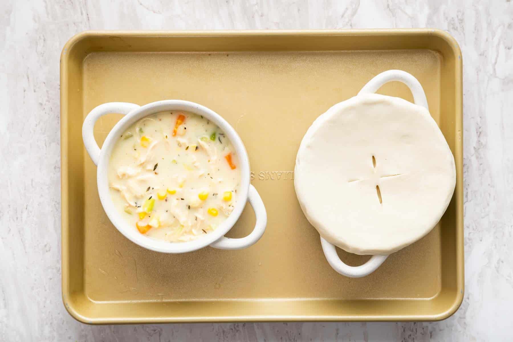Two bowls of chicken pot pie with raw pastry on top of one.