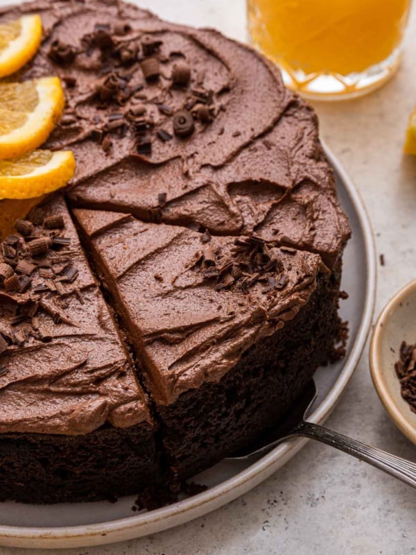 Close up of one layer chocolate orange cake with fudge frosting and a slice being cut.