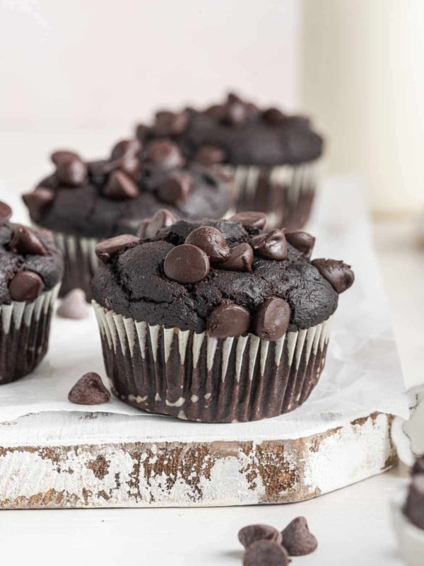 A dark brown chocolate pumpkin muffin topped with chocolate chips on white board.