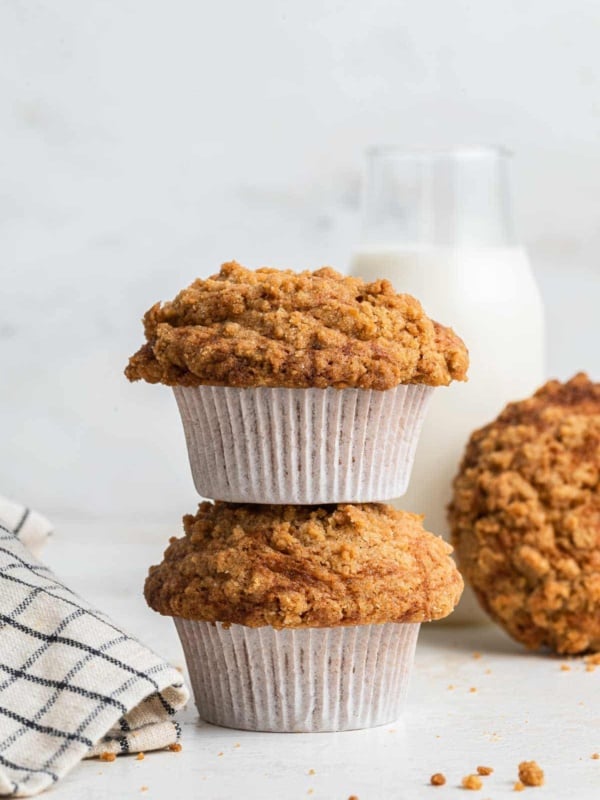 Two crumb topped coffee cake muffins stacked on top of each other with kitchen towel alongside.