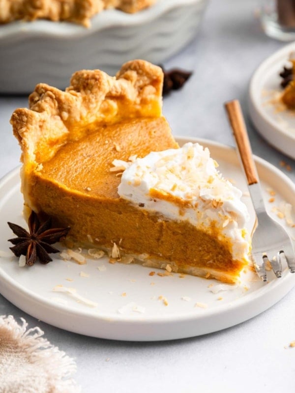 Slice of dairy free pumpkin pie on a plate decorated with coconut whipped cream.