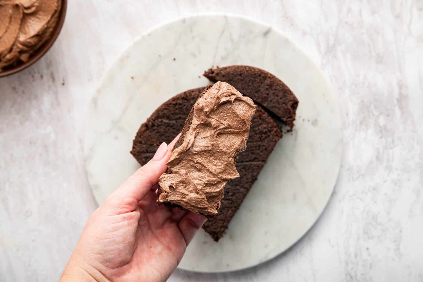 Hand smearing frosting on a piece of baked dessert.