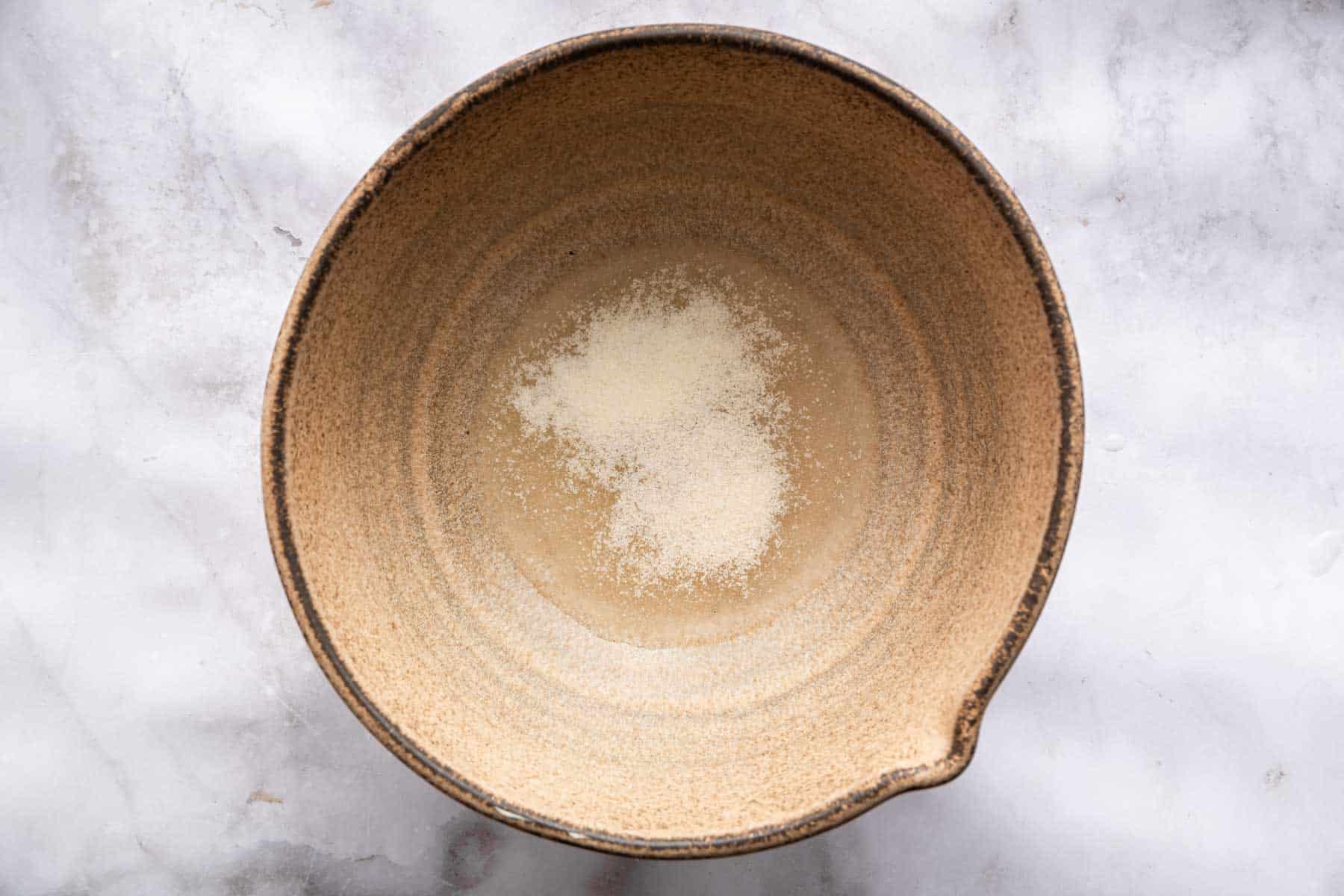 Blooming gelatin in cold water in brown bowl.