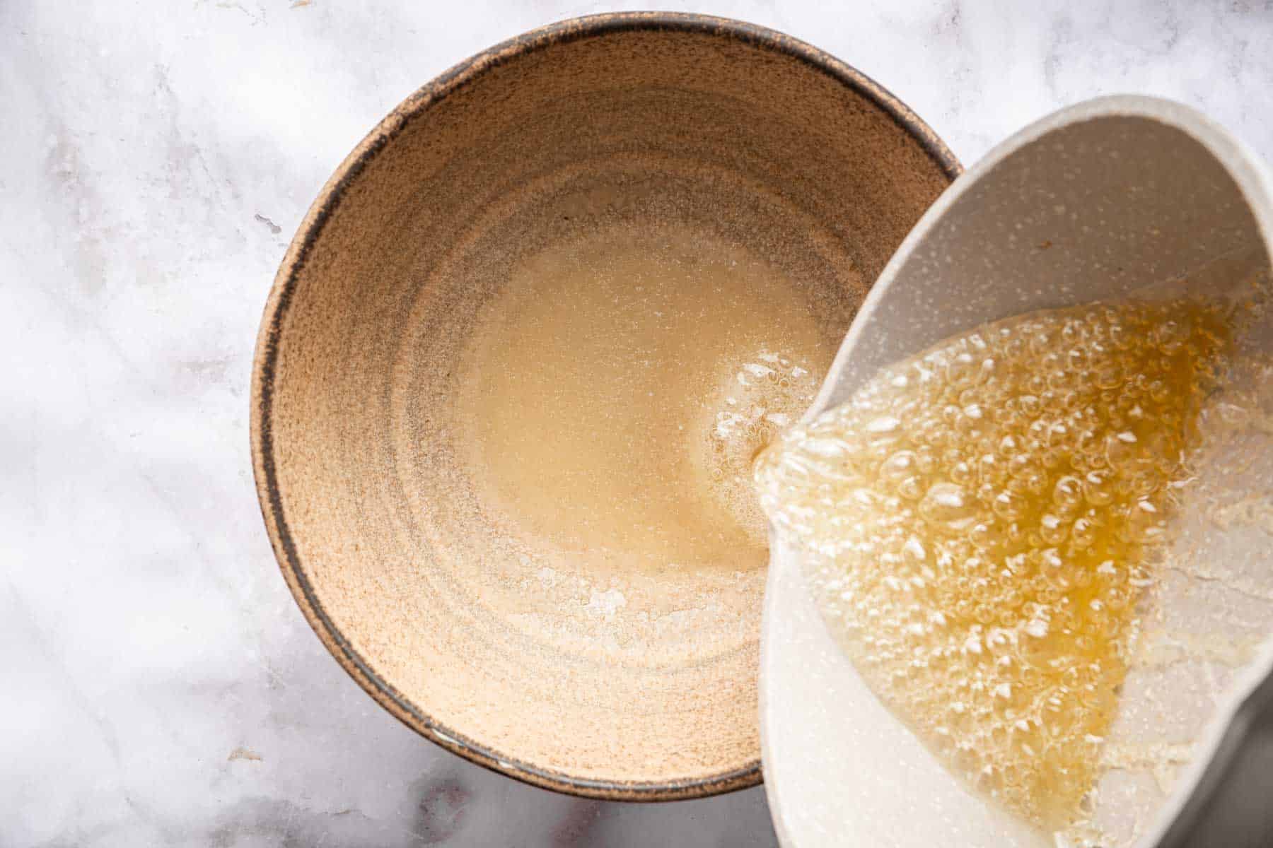 Pouring boiling sugar into bloomed gelatin in a brown bowl.