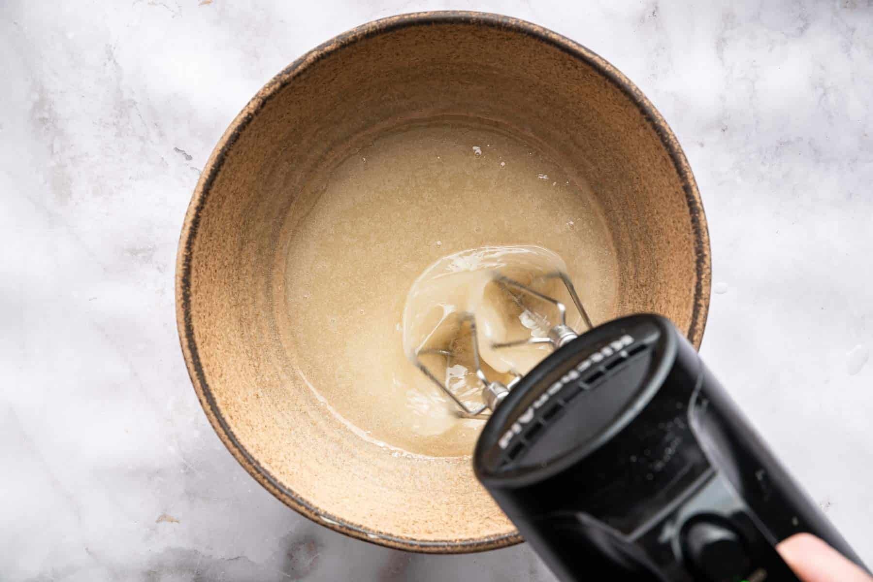 Black hand mixer blending tan cream in bowl.