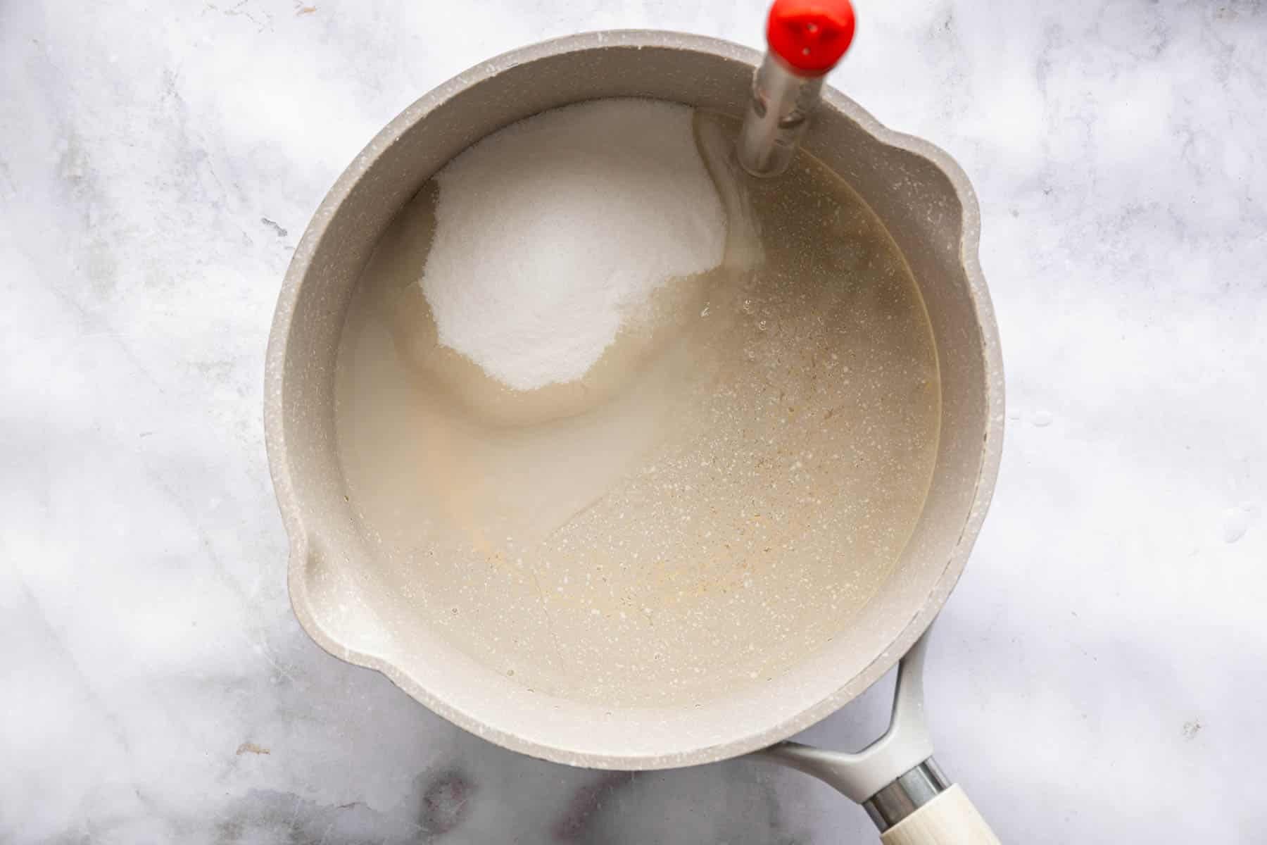 Saucepan with sugar, water and red thermometer clipped to the side.