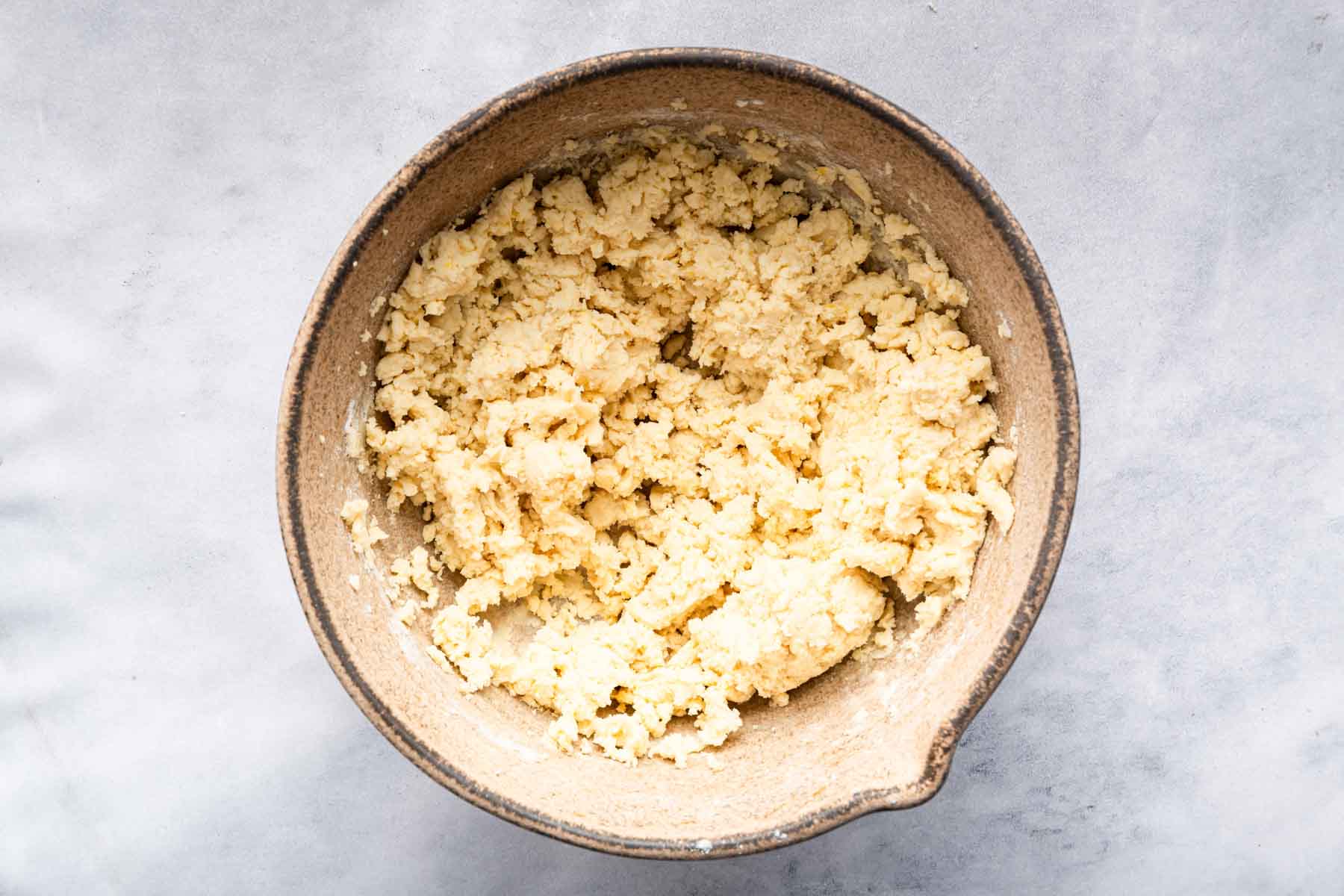 Pale yellow golden cookie dough in a brown clay bowl.