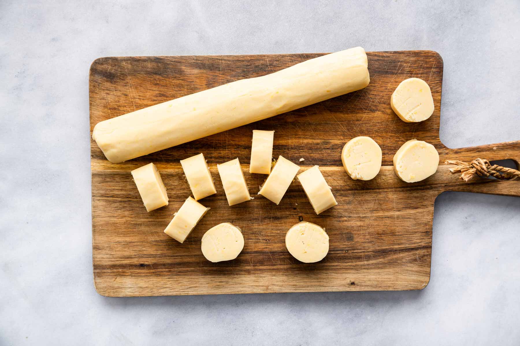 Skinny log of dough sliced on a wooden cutting board.
