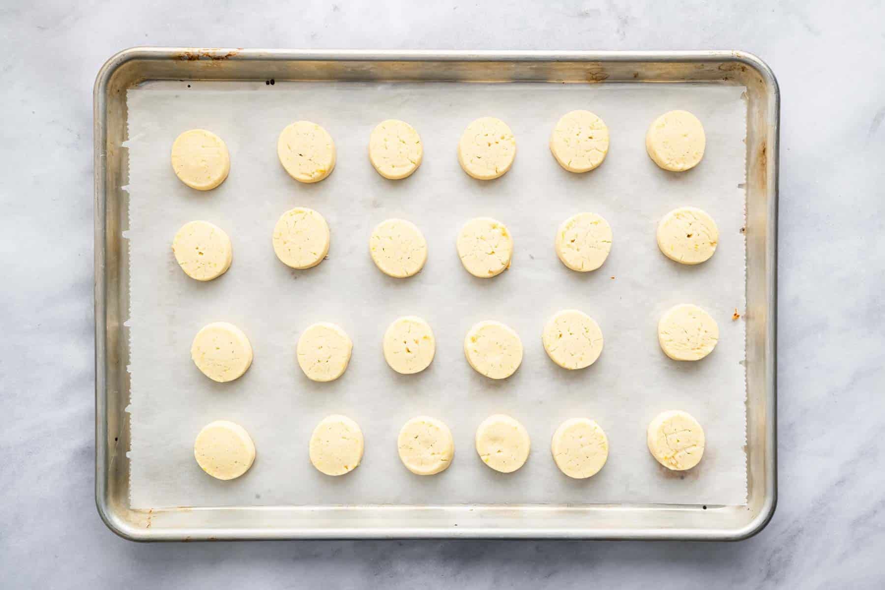 Twenty four yellow small circle cookies on a baking sheet lined with parchment paper.
