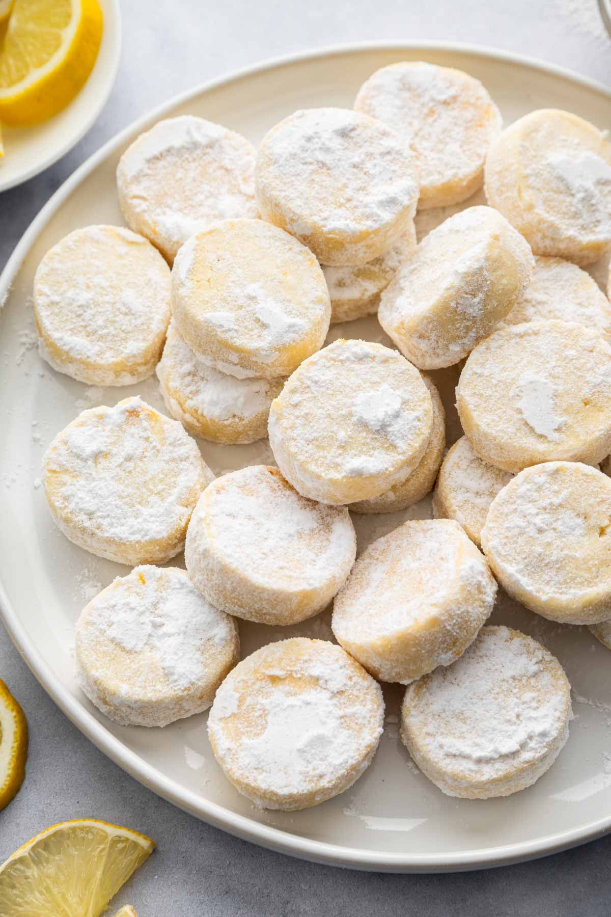 Lemon meltaway cookies on a white plate with lemon slices nearby.