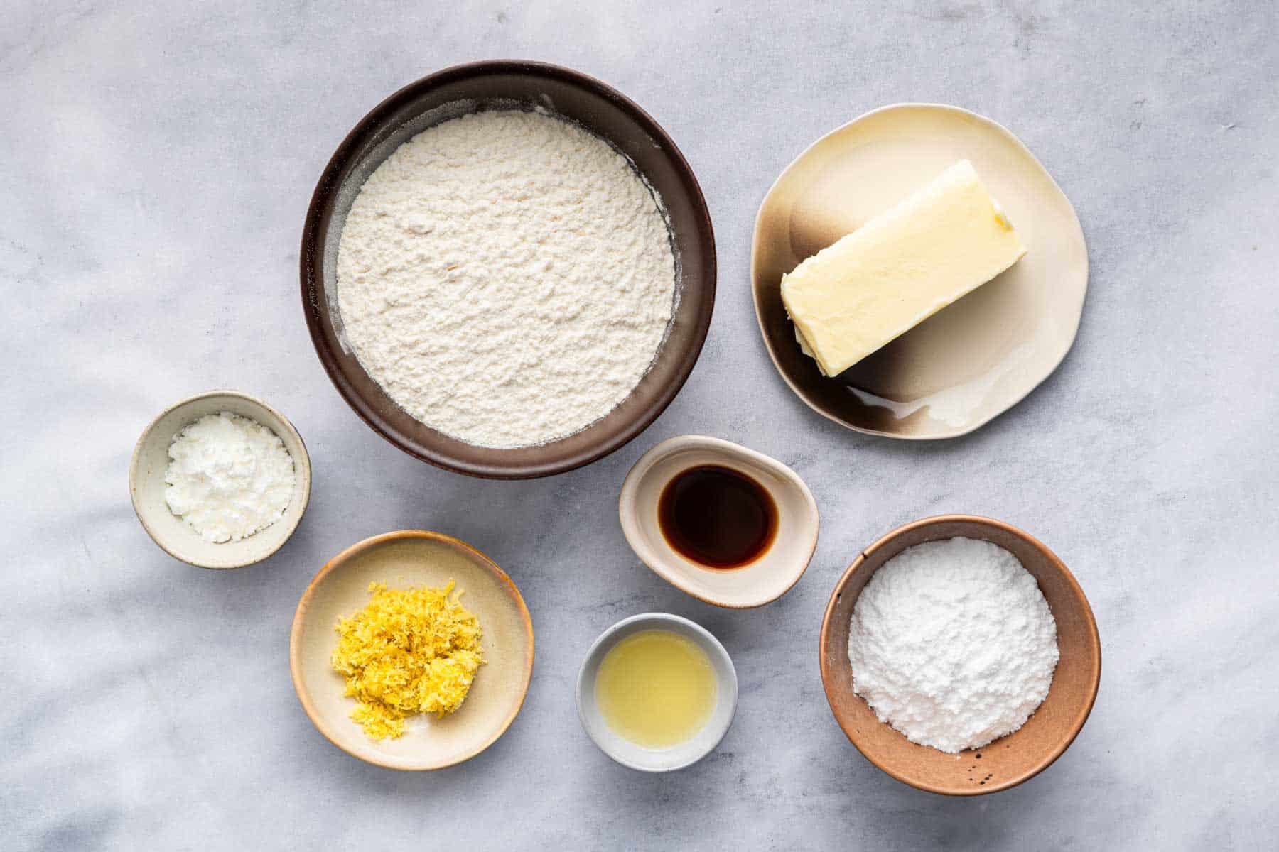 Bowl of flour, lemon zest, butter, and vanilla on marble counter.