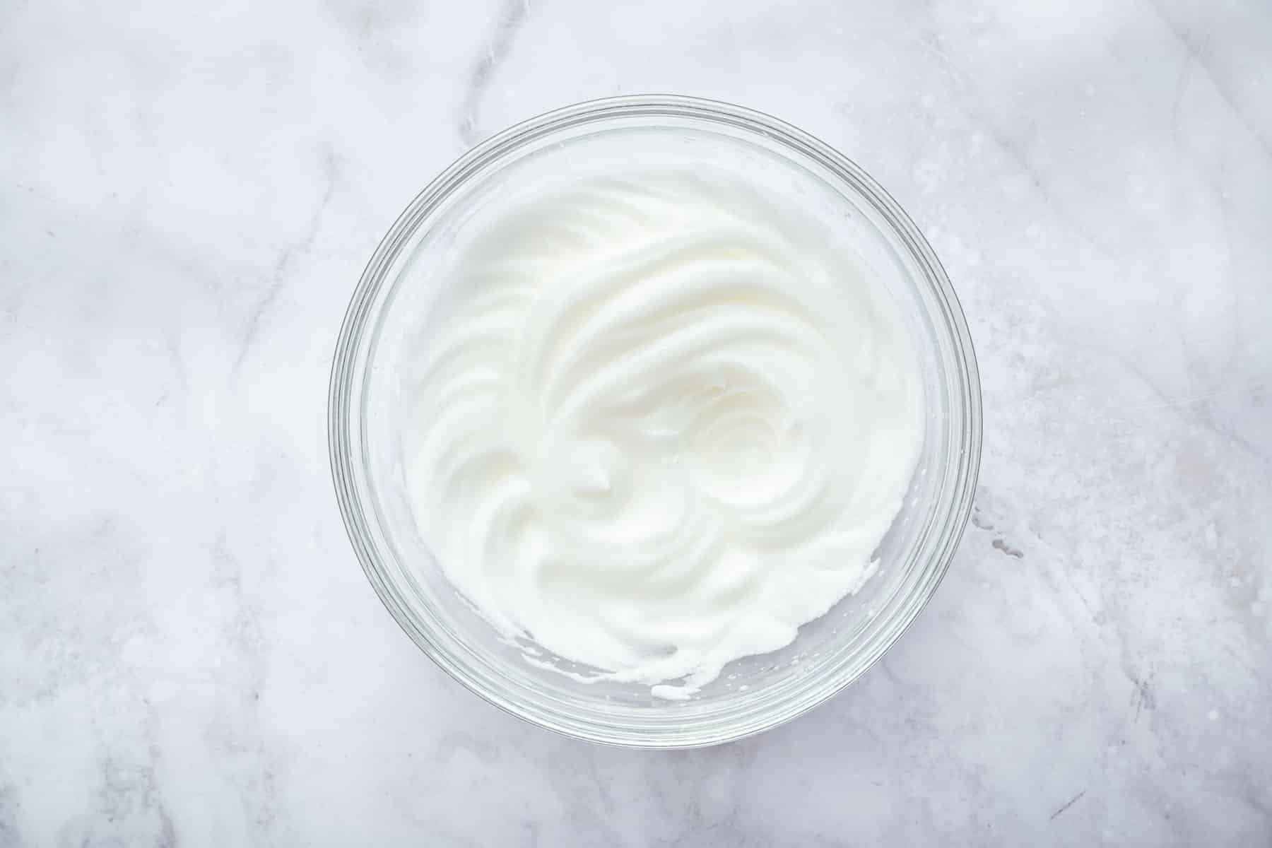 Freshly whipped raw egg white in a clear bowl.