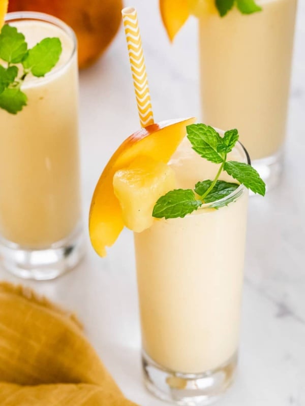 Mango pineapple smoothie in glasses garnished with mint.