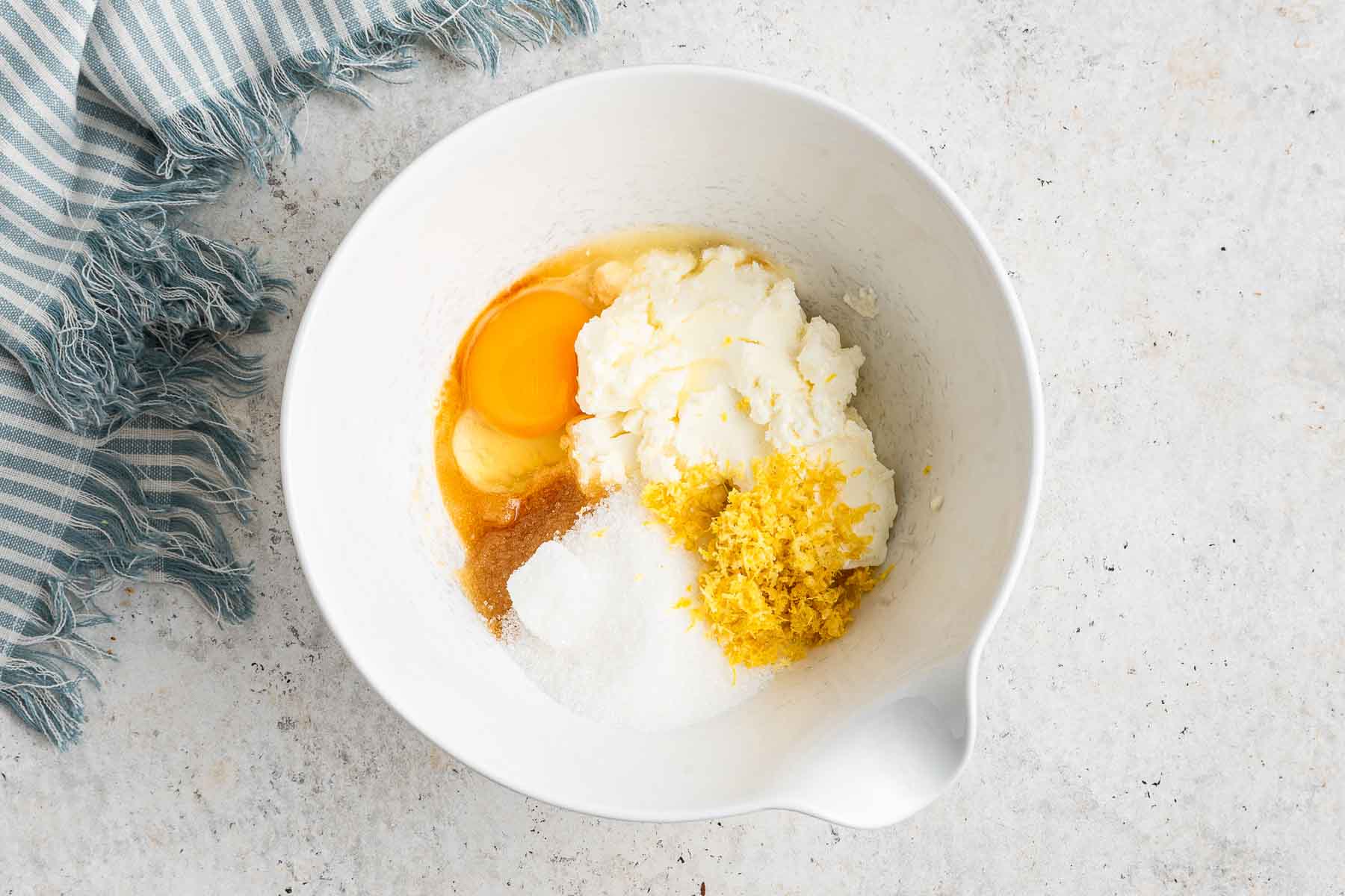 A white bowl with cream cheese, egg, sugar, vanilla and lemon zest before beating.