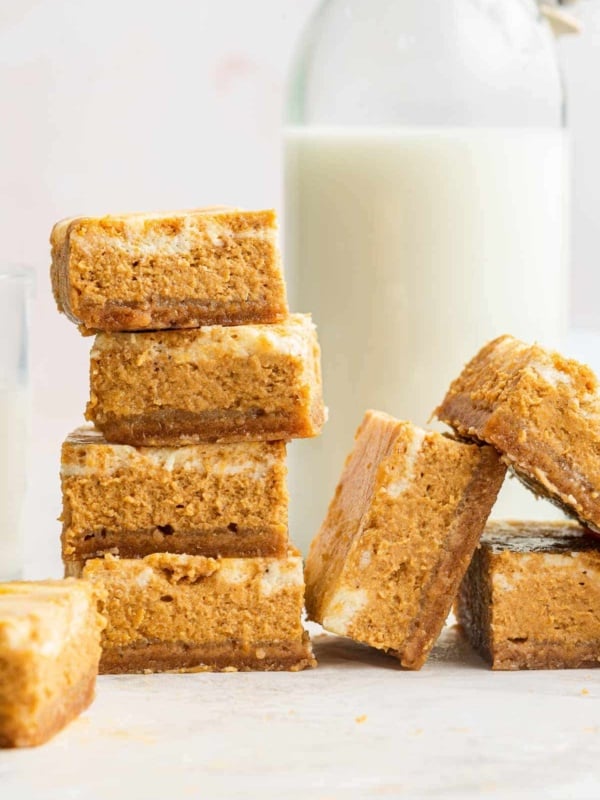 Stacks of pumpkin cheesecake bars with swirled top and glass of milk.