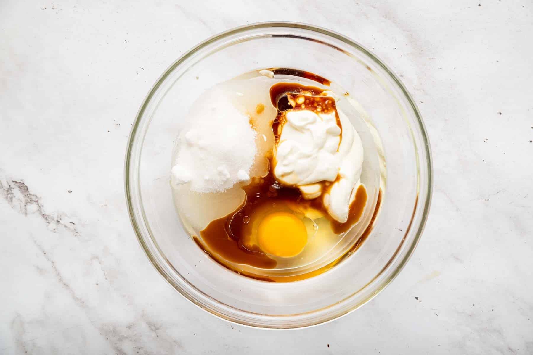 Clear glass bowl with sour cream, egg, sugar and vanilla splashes.