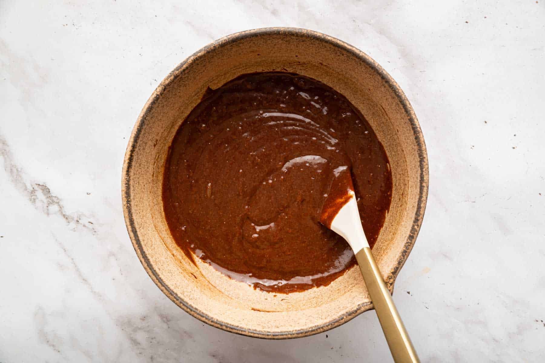 Shiny brown cake batter with white spatula in it.
