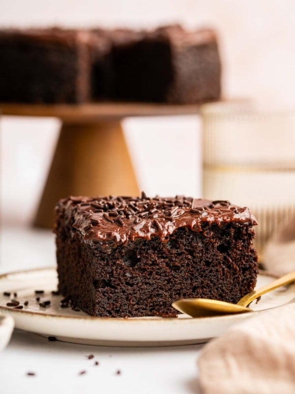 Vertical image of slice of sour cream chocolate cake with whole cake behind it.
