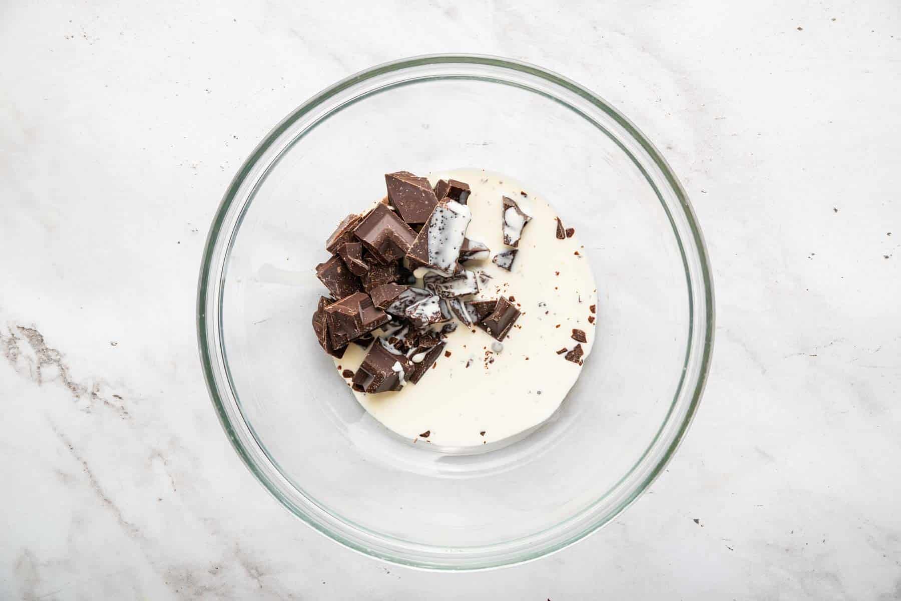 Clear glass bowl with cream and chopped chocolate pieces.