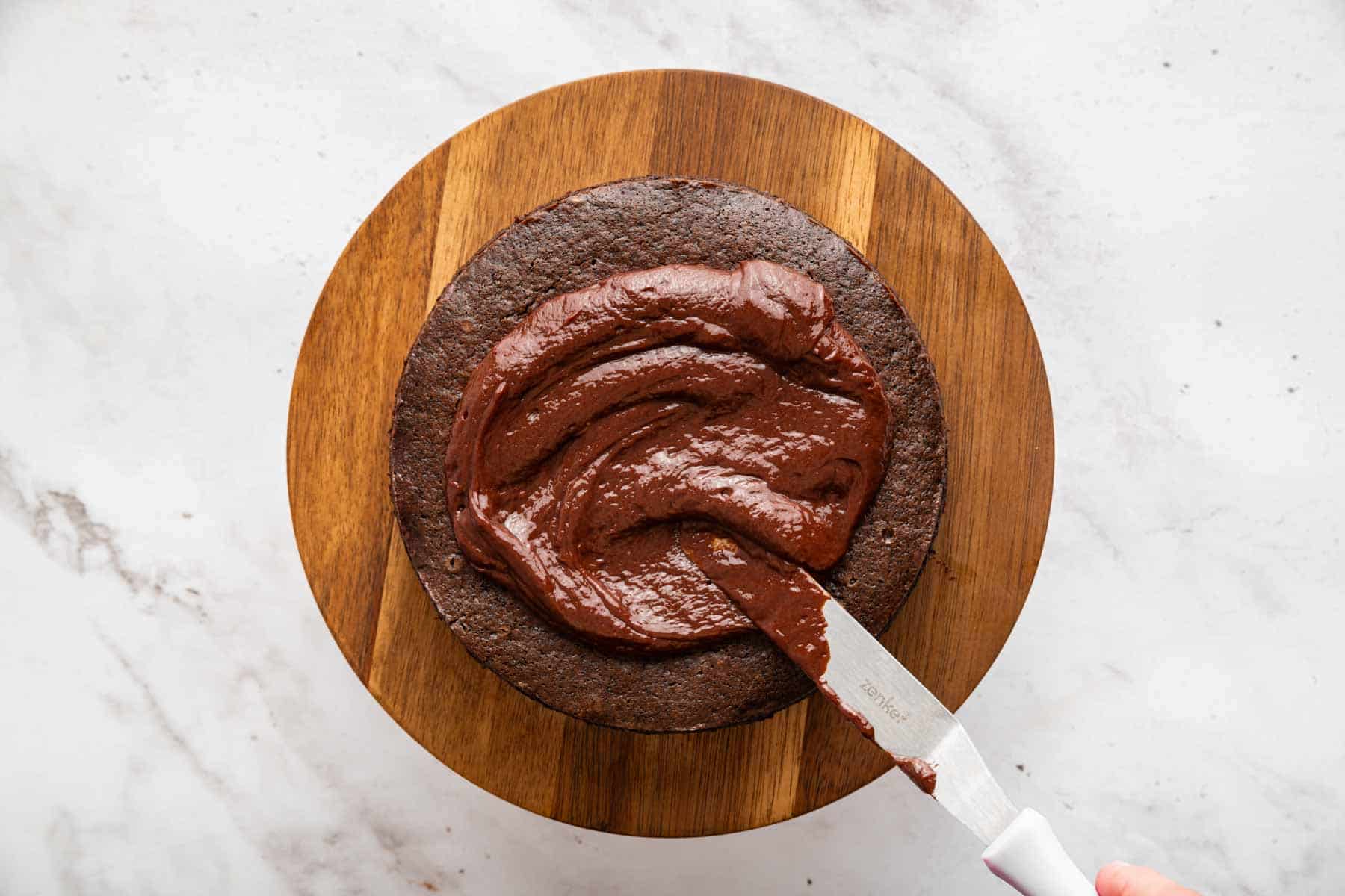 Knife spreading ganache on a small cake.