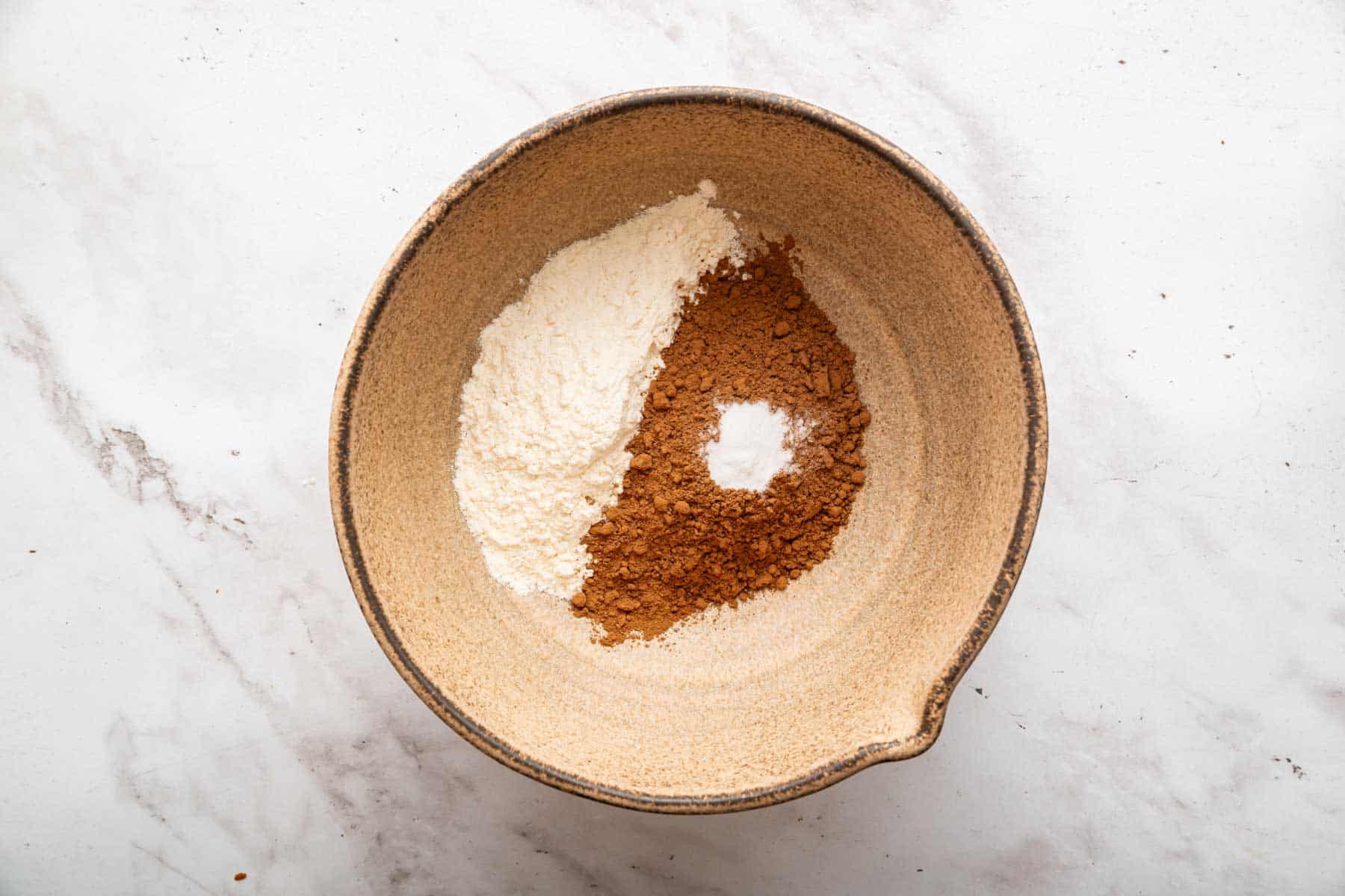 Brown bowl with half flour, half cocoa powder and a small amount of baking soda.