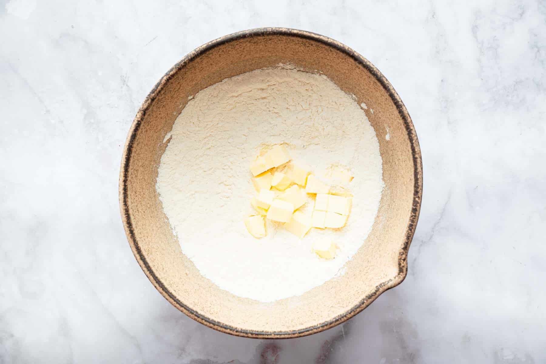 Brown pottery bowl with flour mixture and diced butter in center.