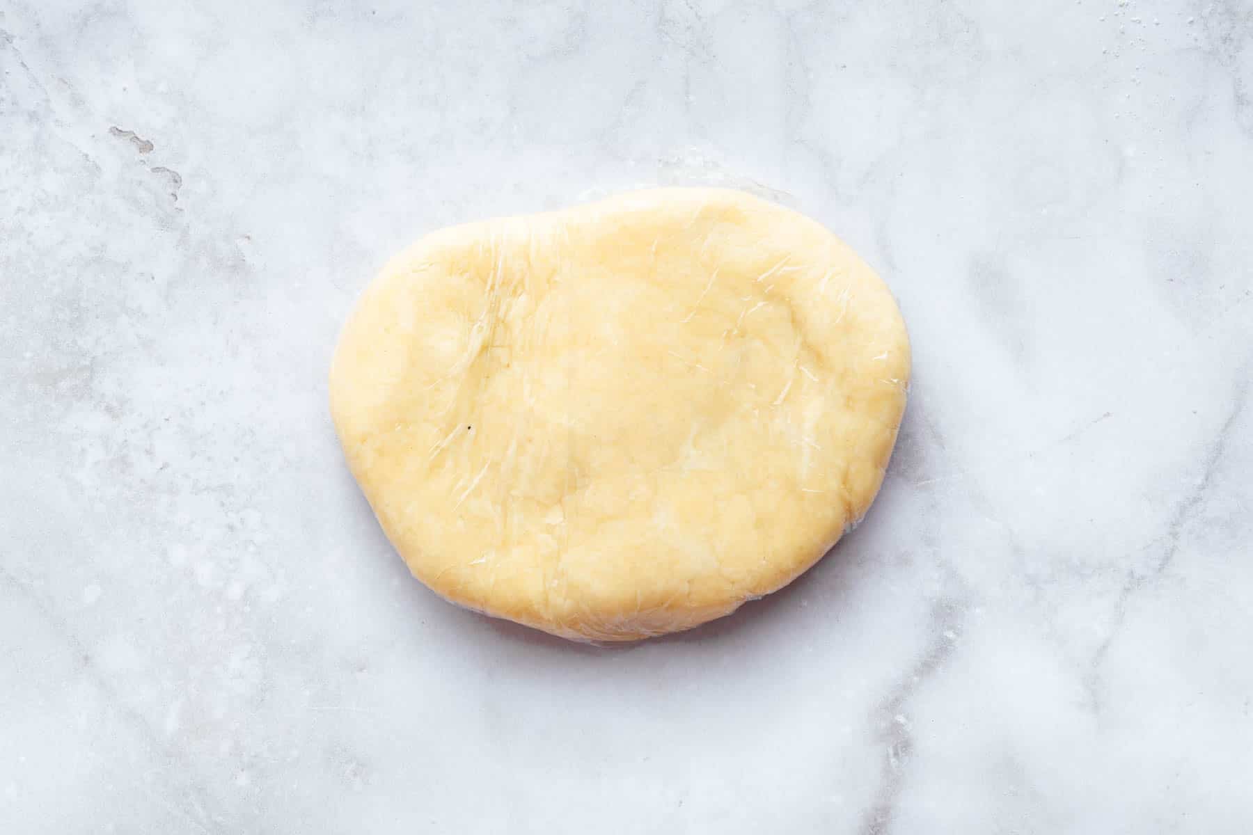 Pale yellow pastry dough oval on marble surface.