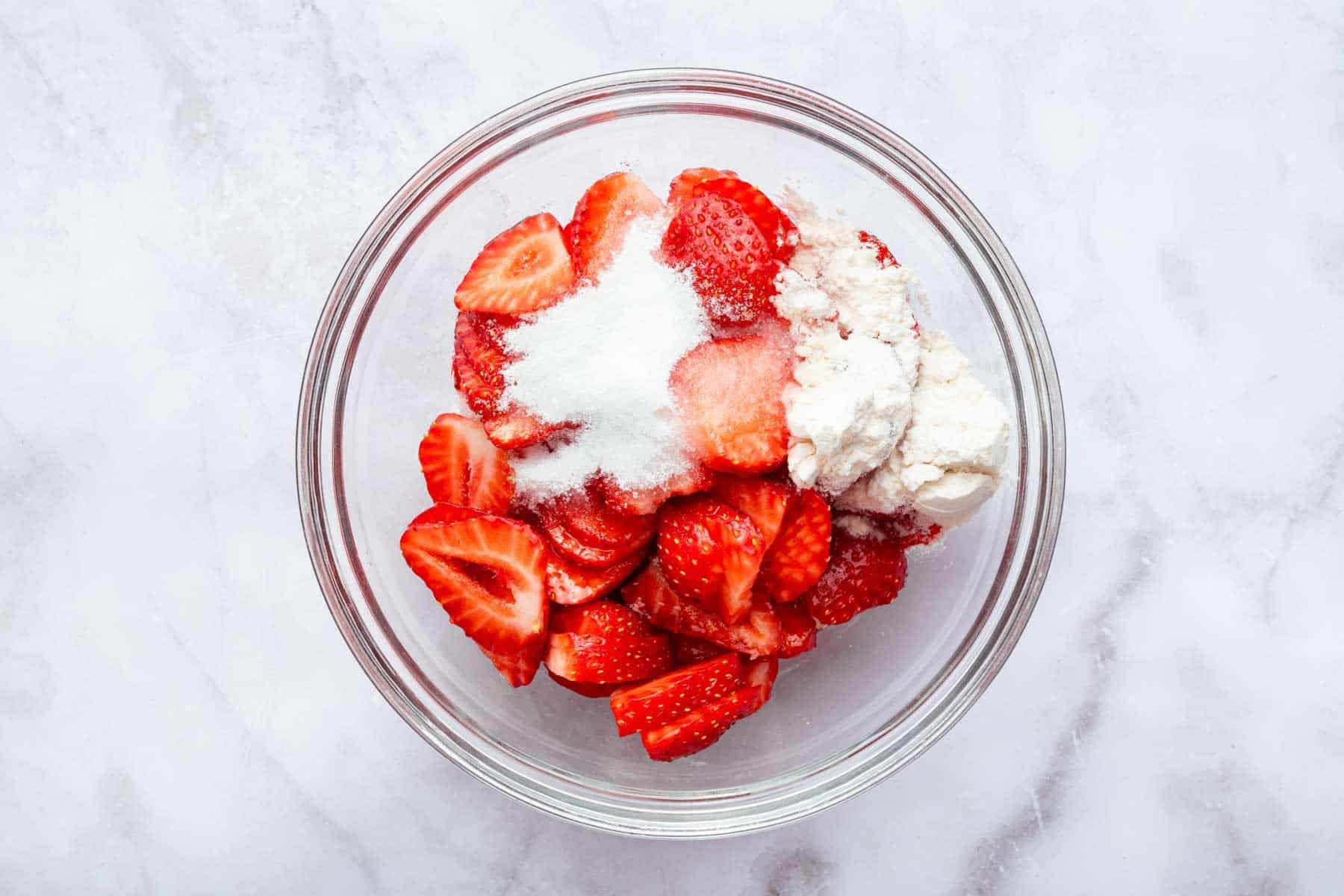 Glass bowl with sliced strawberries with flour and sugar on top.