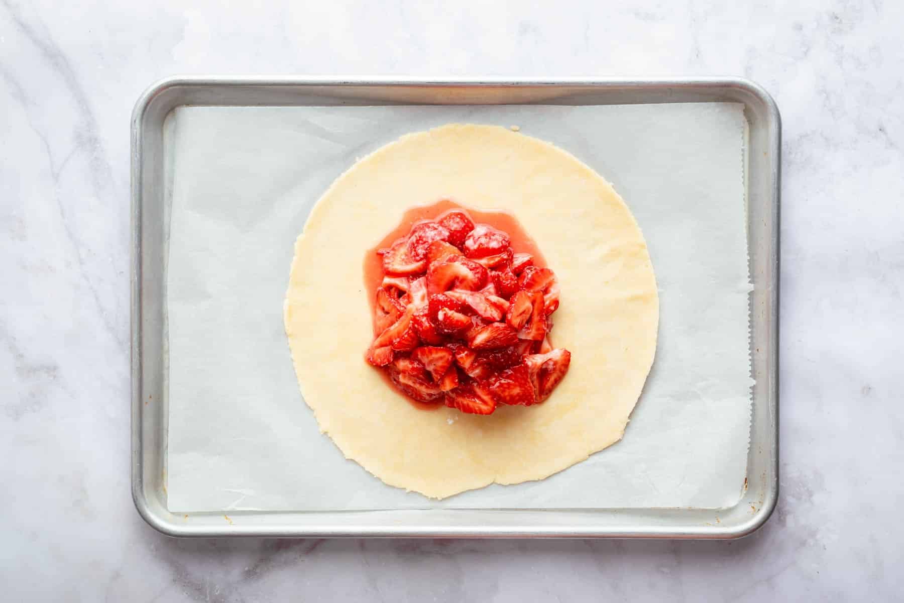 Dough circle with sliced wet strawberries piled in center.