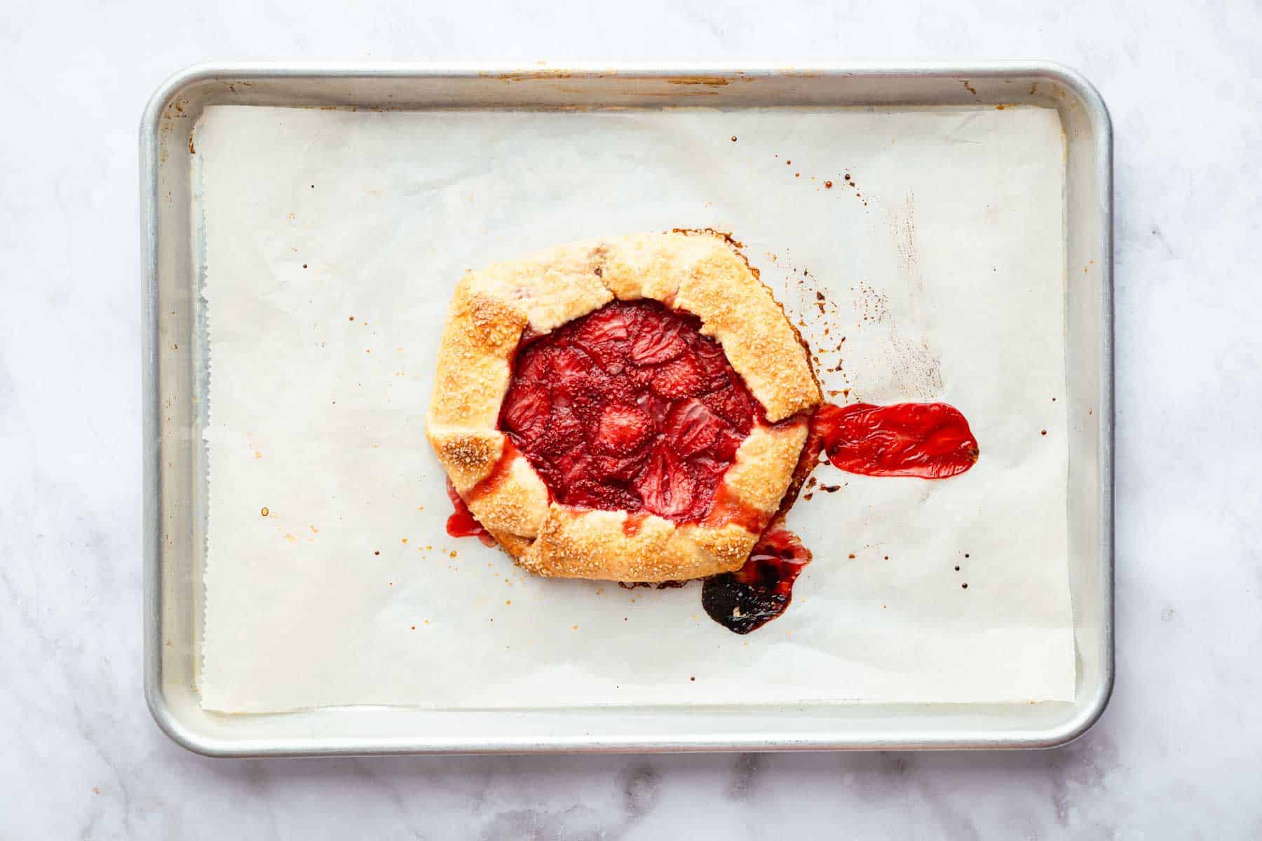 Baked strawberry galette on baking sheet with fresh juices leaking out.