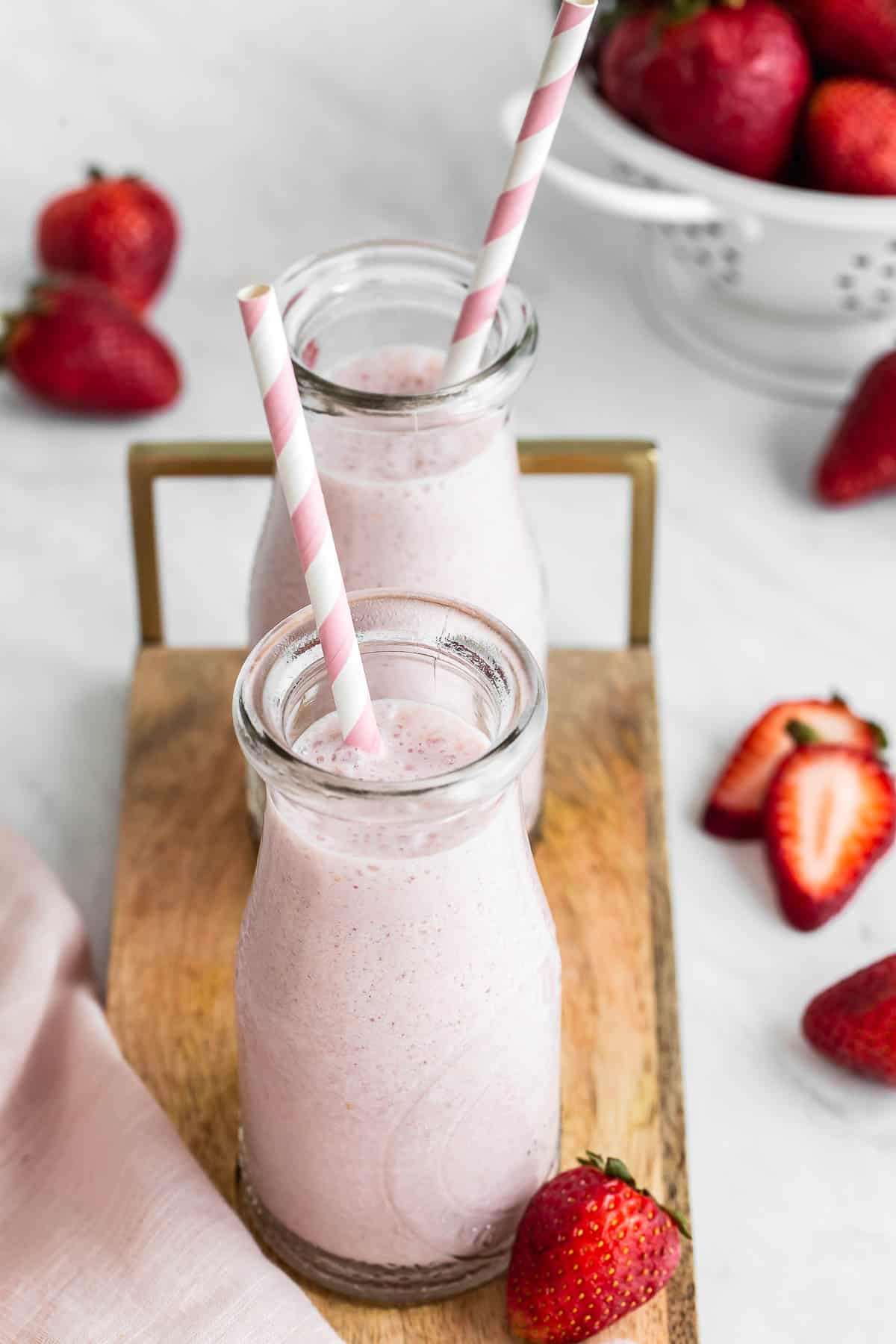 Two glasses of strawberry milk with straws.