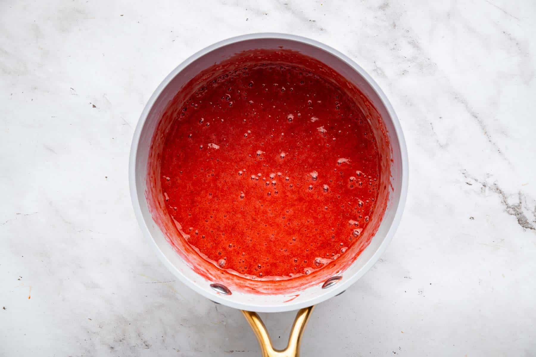 Bright red fruit sauce puree in grey skillet.