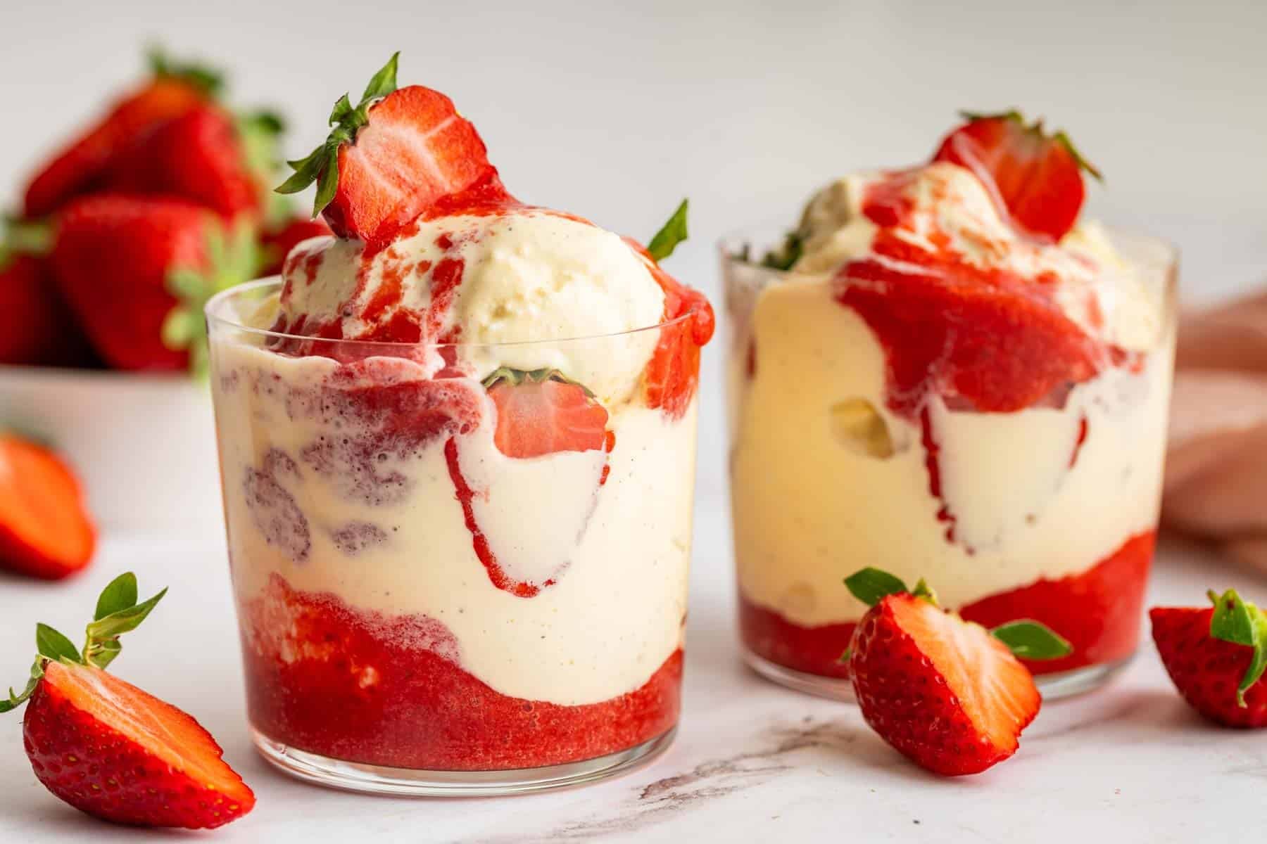 Horizontal image of two strawberry sundaes with fresh strawberries on top.