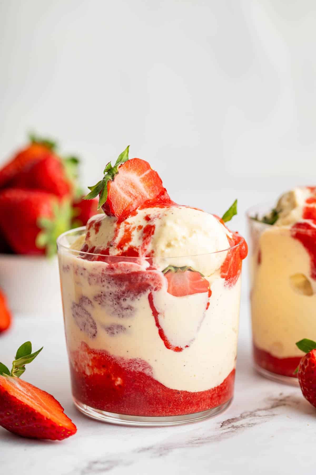 Two glass cups full of vanilla ice cream and fresh strawberry sauce sundae.