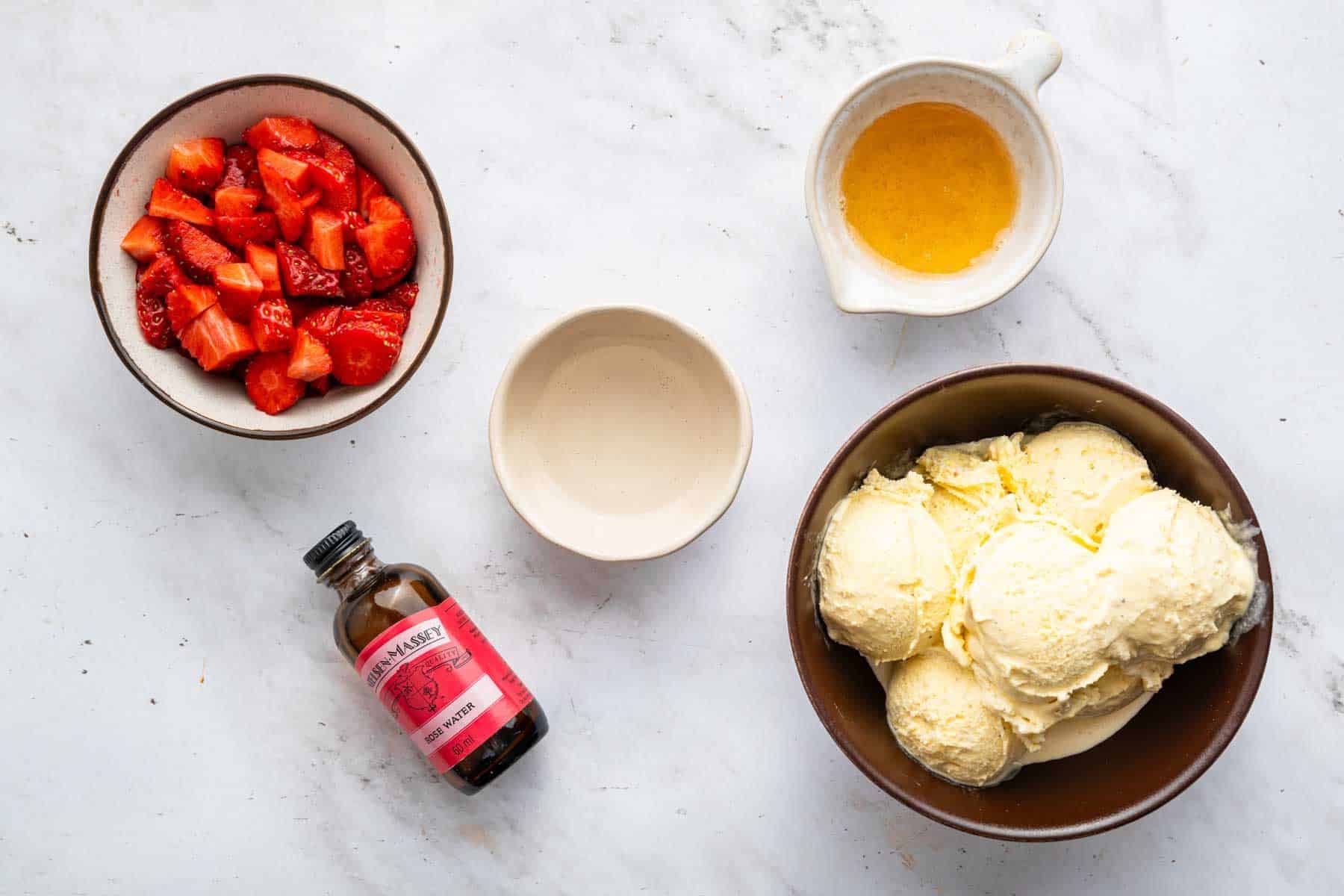 Bowl of chopped fruit, scoops of ice cream, and rose water bottle.