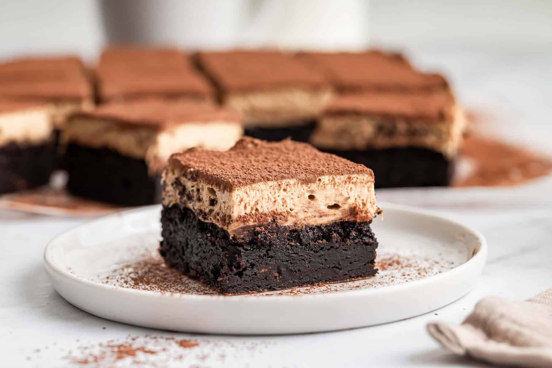 Horizontal image of layered tiramisu brownie on white plate.
