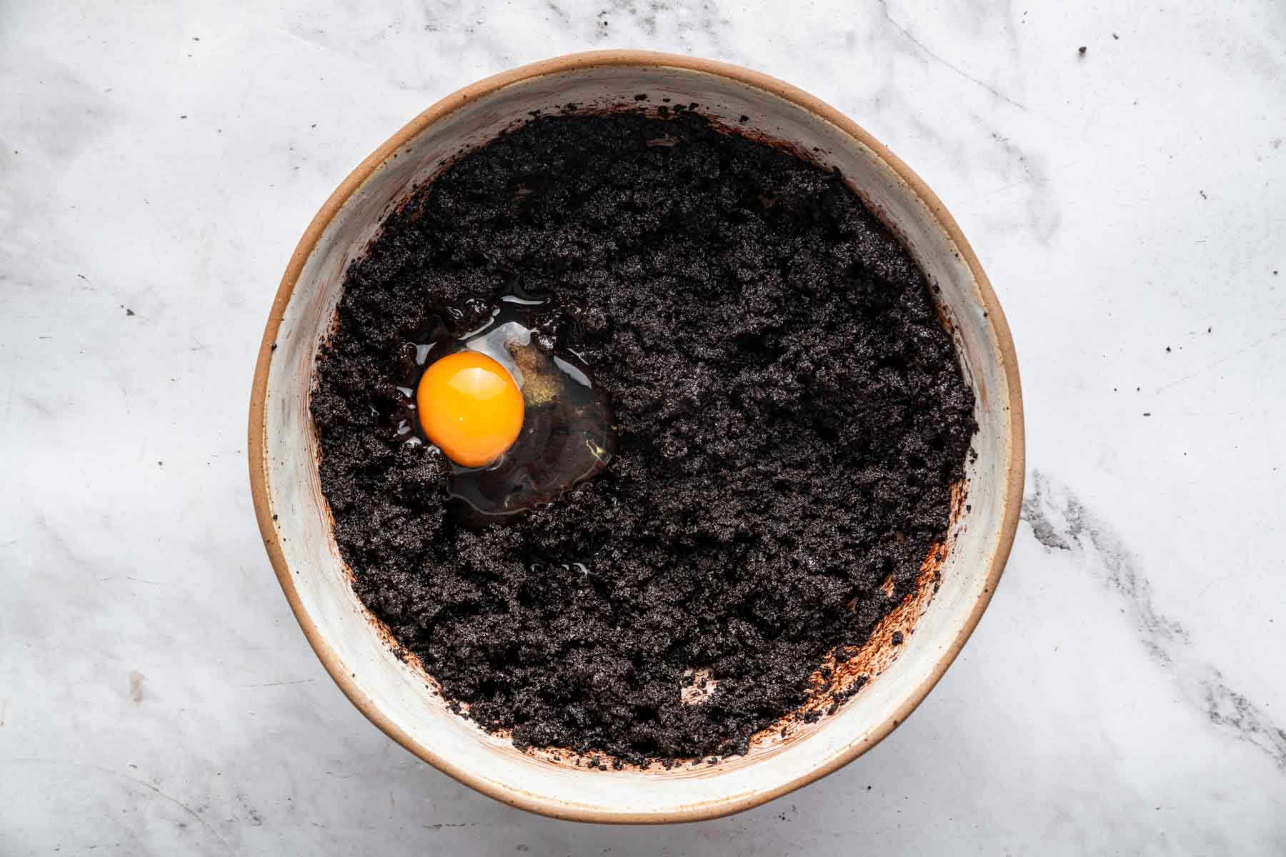Dark brown wet grainy batter with egg on top.