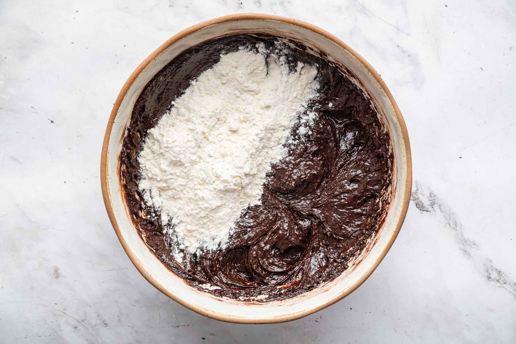 White flour sprinkled over dark brownie batter.