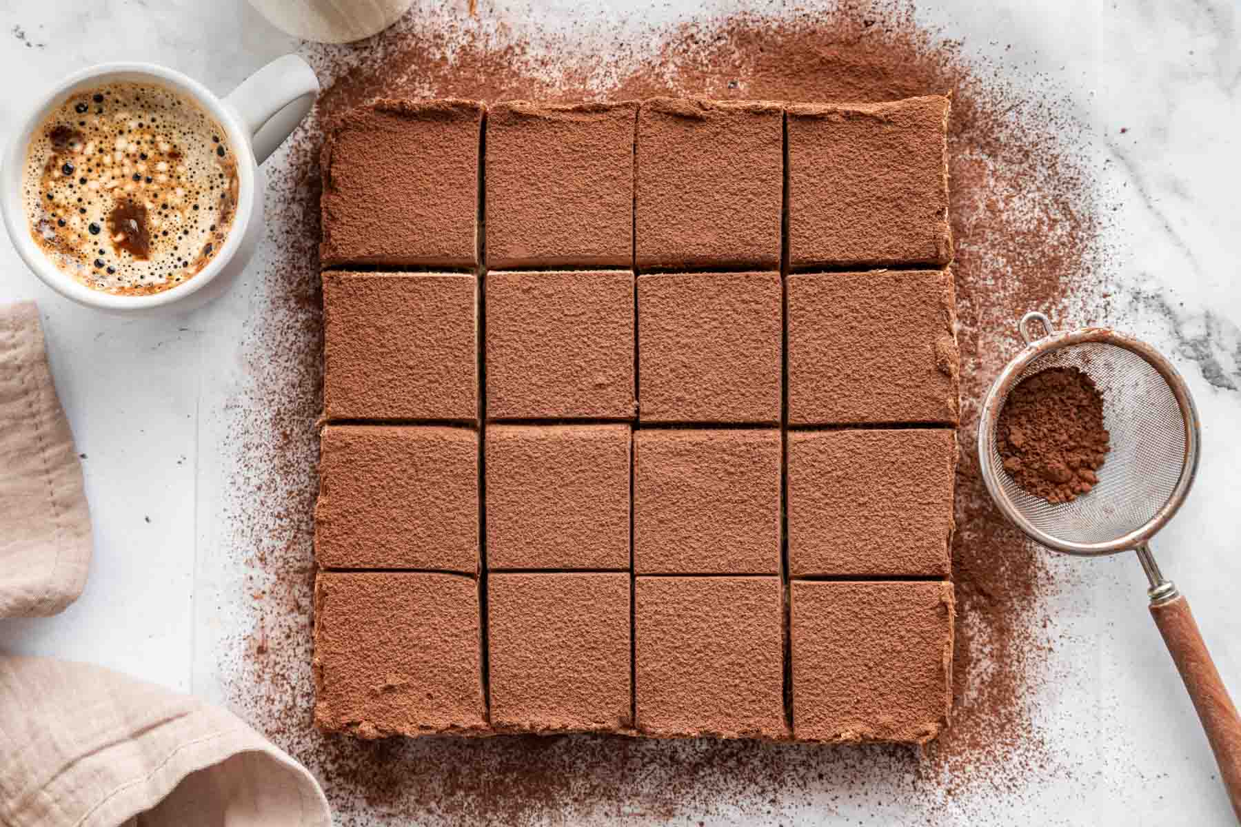 Square pan of tiramisu brownies decorated with cocoa powder and sliced.