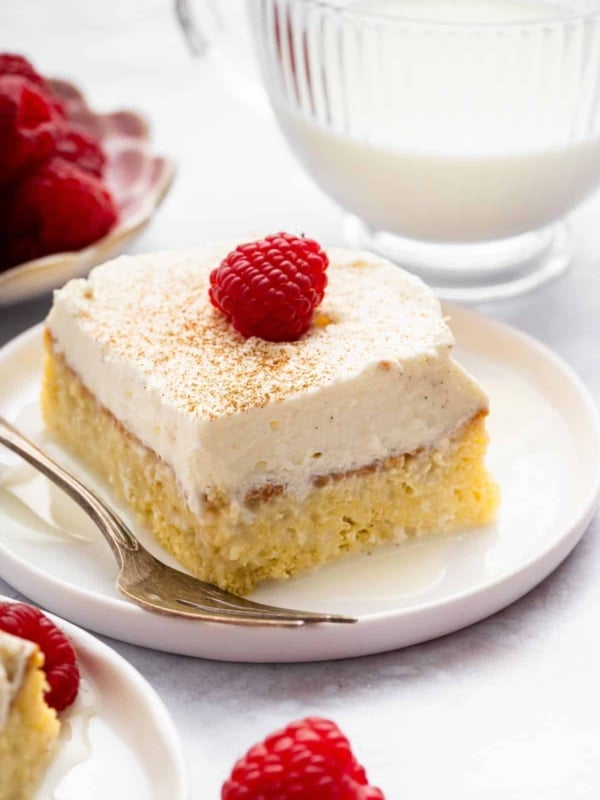 Square slice of tres leches cake recipe with raspberry on top.