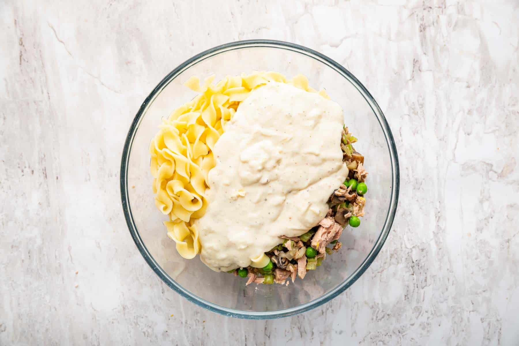 Bowl with white sauce, cooked pasta, and veggies.