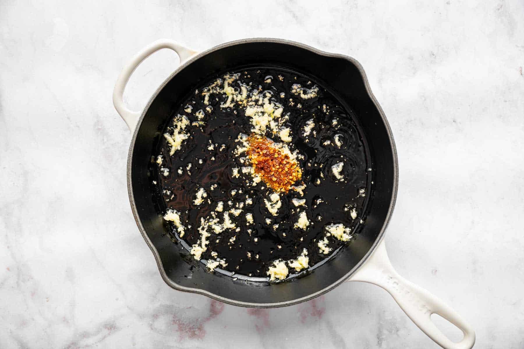 Black skillet with minced garlic and red pepper flakes.